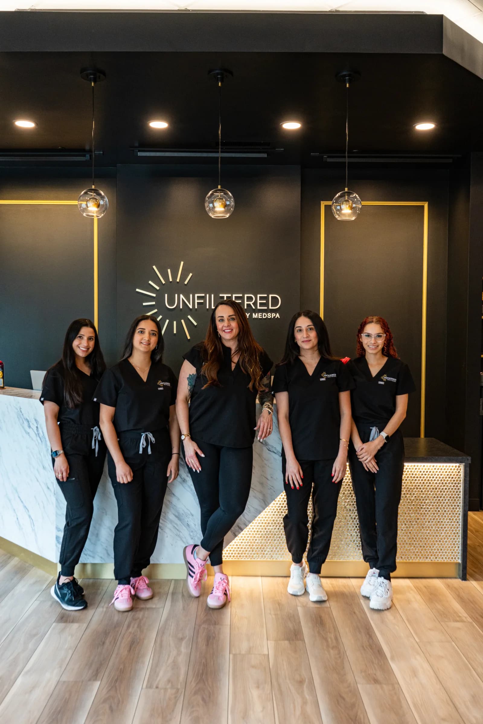 The Unfiltered Beauty MedSpa team together in front of the reception wall