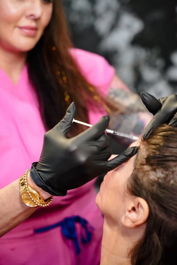 A provider in pink scrubs and black gloves giving a client an injection at the brow