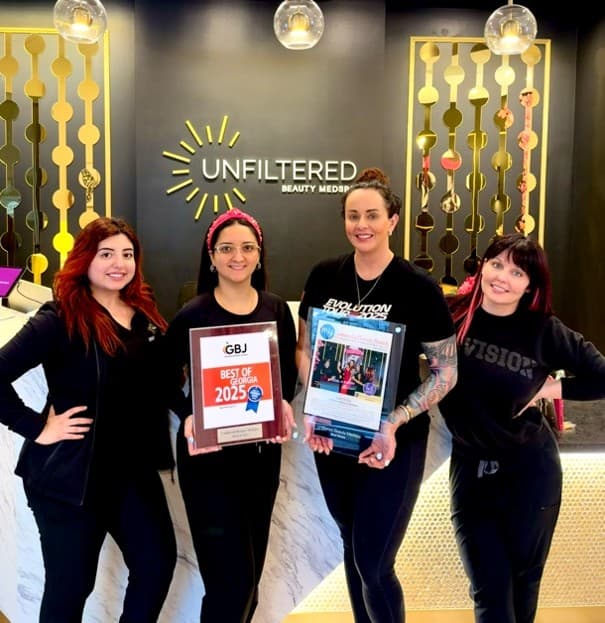Four of the Unfiltered Beauty MedSpa team holding their Best of Georgia and Best Self award plaques, under the studio's logo wall