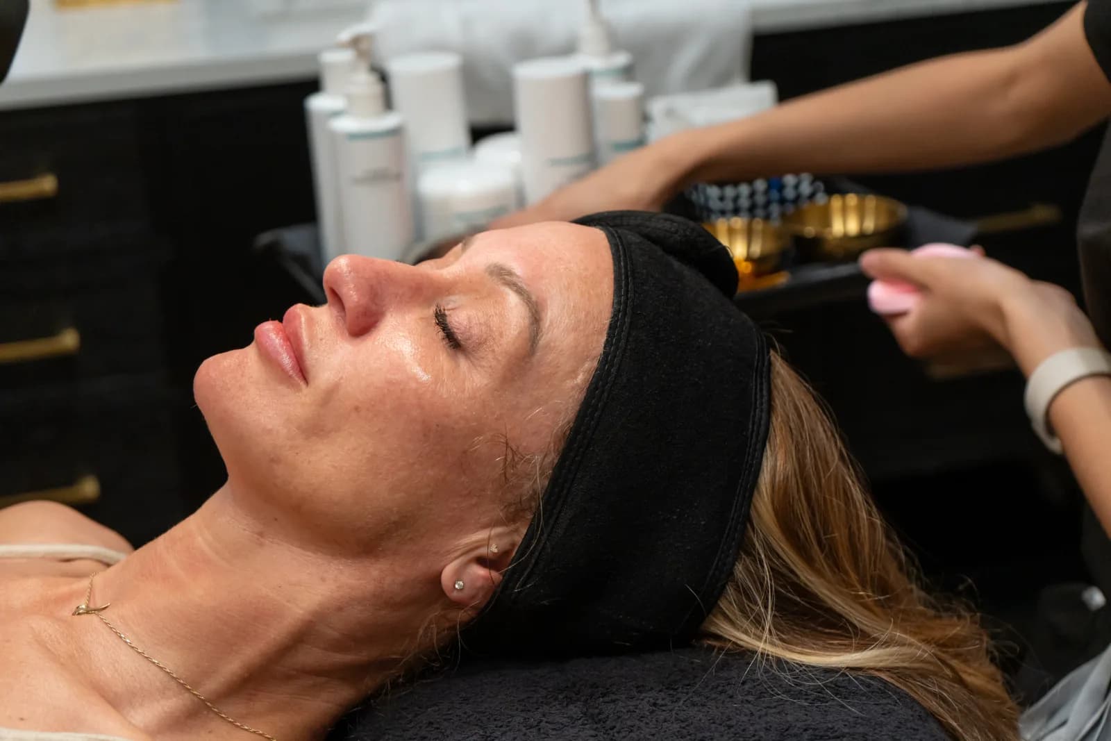 A client resting during a facial, the product shelf behind her