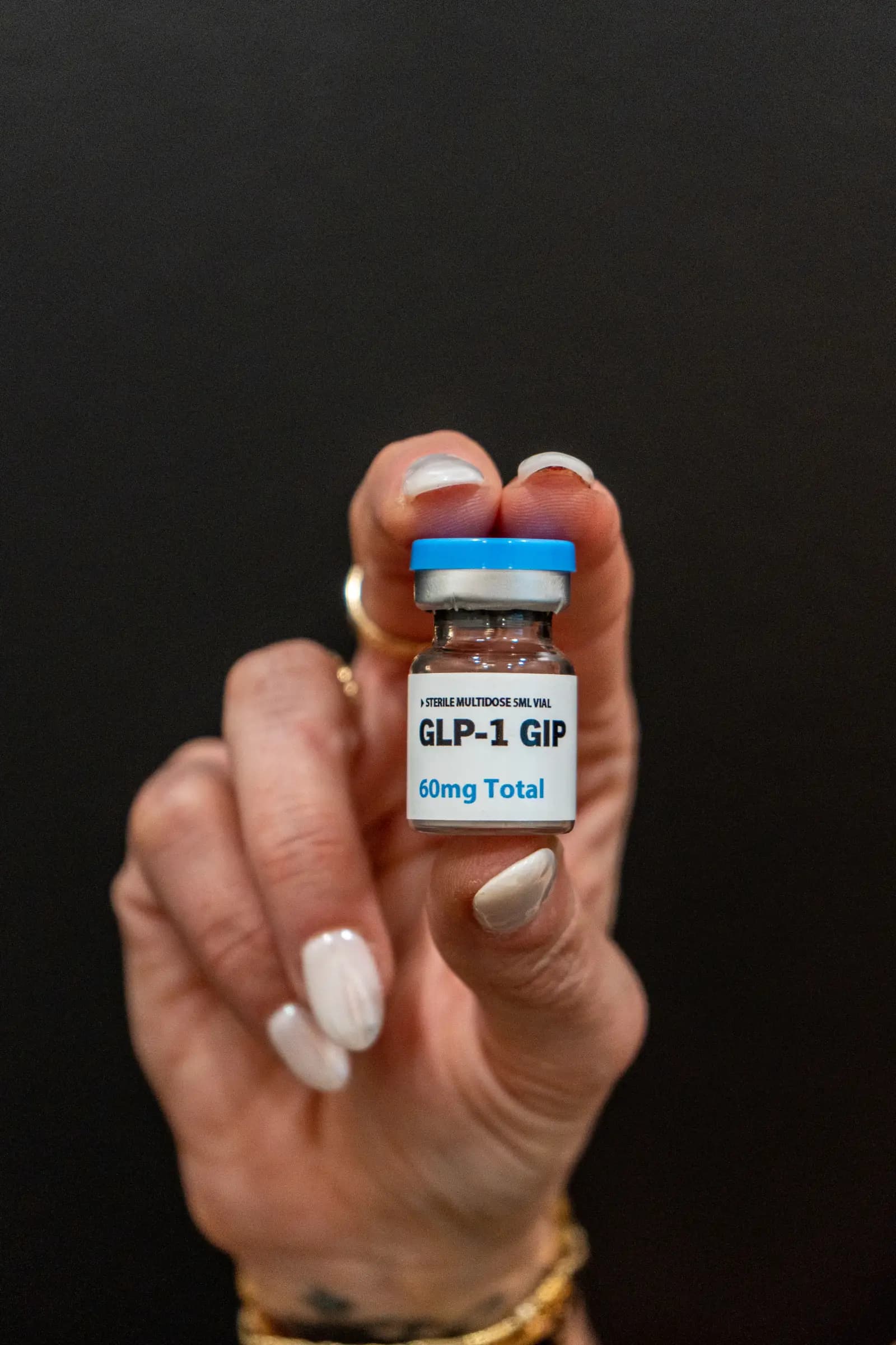 A labelled GLP-1 GIP medication vial held in a gloved hand